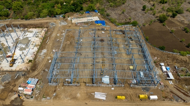 Aerial view of a warehouse construction site featuring a large steel frame structure heavy machinery and cranes on a dirt lot in Bhiwandi Maharashtra India. Aerial view of a warehouse construction site featuring a large steel frame structure heavy machinery and cranes on a dirt lot in Bhiwandi Maharashtra India.