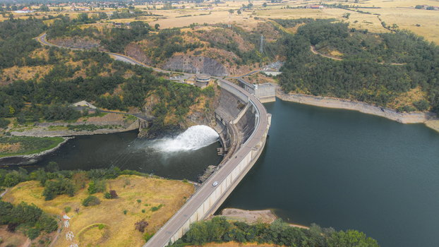 Aerial view of the Barrage de Villerest dam with water discharging into the river surrounded by lush green forests and dry golden fields Commelle Vernay Auvergne Rhone Alpes France. Aerial view of the Barrage de Villerest dam with water discharging into the river surrounded by lush green forests and dry golden fields Commelle Vernay Auvergne Rhone Alpes France.