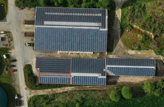 Aerial view of solar panels on industrial rooftops surrounded by lush greenery and dirt roads in Hofgeismar Hessen Germany. Aerial view of solar panels on industrial rooftops surrounded by lush greenery and dirt roads in Hofgeismar Hessen Germany.