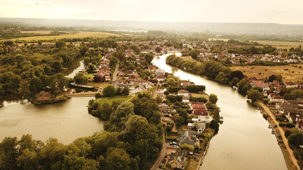 Aerial view of the Thames River winding through a residential town with lush trees green spaces and houses in Thames United Kingdom. Aerial view of the Thames River winding through a residential town with lush trees green spaces and houses in Thames United Kingdom.