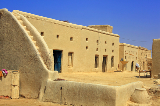 View of the traditional mud brick architecture of the Chanan Pir shrine complex with its distinctive curved staircase and blue door in Yazman Punjab Pakistan.