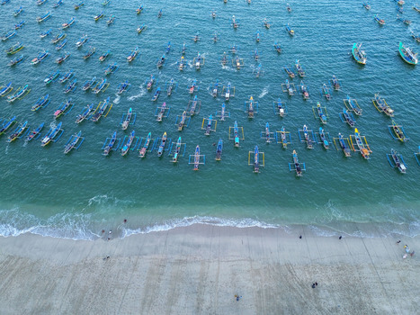 Aerial view of Papuma Beach with numerous traditional fishing boats anchored in the turquoise sea along the sandy coastline in Jember East Java Indonesia. Aerial view of Papuma Beach with numerous traditional fishing boats anchored in the turquoise sea along the sandy coastline in Jember East Java Indonesia.