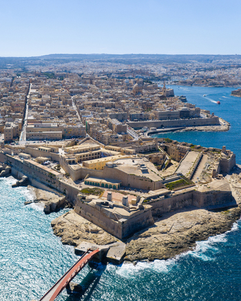 Aerial view of Fort Saint Elmo and the historic city of Valletta featuring limestone fortifications dense urban rooftops and the Mediterranean Sea in Valletta Port Region Malta. Aerial view of Fort Saint Elmo and the historic city of Valletta featuring limestone fortifications dense urban rooftops and the Mediterranean Sea in Valletta Port Region Malta.