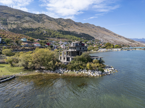 Aerial view of an unfinished concrete building situated on the rocky shore of Lake Shkoder surrounded by trees and mountains in the background in Shiroka Shkoder County Albania. Aerial view of an unfinished concrete building situated on the rocky shore of Lake Shkoder surrounded by trees and mountains in the background in Shiroka Shkoder County Albania.