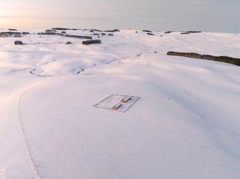 Aerial view of a snow blanketed landscape dotted with dark trees and two small typical houses called burons Nasbinals Occitanie France.
