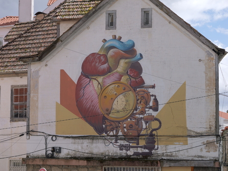 View of a mural depicting an anatomical heart integrated with clockwork gears on the side of a white building in Covilha Castelo Branco Portugal.
