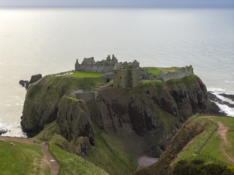Aerial view of Dunnottar Castle ruins perched on a dramatic cliff overlooking the North Sea with green grass and steep rocky slopes Stonehaven Scotland United Kingdom. Aerial view of Dunnottar Castle ruins perched on a dramatic cliff overlooking the North Sea with green grass and steep rocky slopes Stonehaven Scotland United Kingdom.