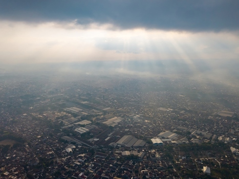 Aerial view of the city of Malang with dense urban rooftops and industrial buildings illuminated by dramatic sun rays breaking through clouds in Malang East Java Indonesia.
