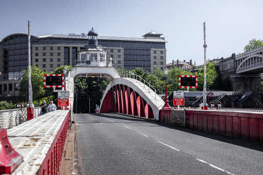 View of the historic Swing Bridge with its distinctive red metal structure and control tower set against the backdrop of the Hilton hotel in Newcastle upon Tyne England United Kingdom. View of the historic Swing Bridge with its distinctive red metal structure and control tower set against the backdrop of the Hilton hotel in Newcastle upon Tyne England United Kingdom.