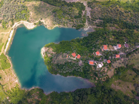 Aerial view of a turquoise lake surrounded by lush green hills and houses with red roofs in Kruje Durres County Albania.