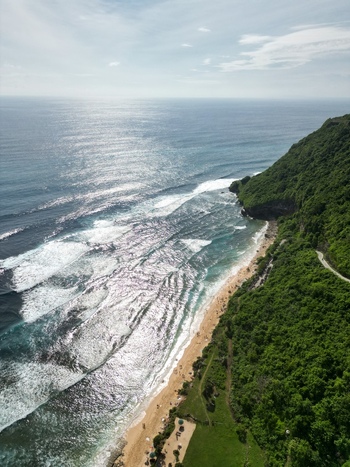 Aerial view of Pantai Nunggalan with its sandy beach crashing waves and lush green cliffs in Kecamatan Kuta Selatan Bali Indonesia.
