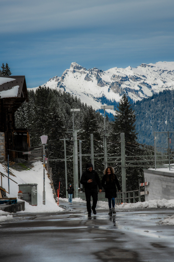 View of a couple walking down a road with snow dusted trees and buildings against a backdrop of majestic snow capped mountains Murren Switzerland. View of a couple walking down a road with snow dusted trees and buildings against a backdrop of majestic snow capped mountains Murren Switzerland.