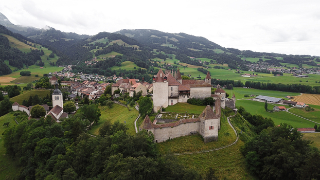 Aerial view of the medieval Chateau de Gruyeres with its fortified walls and gardens overlooking the village and lush green hills under a cloudy sky in Gruyeres Fribourg Switzerland.