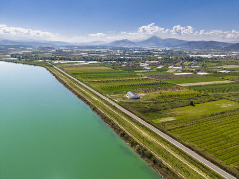 Aerial view of agricultural fields and Liqeni Thanes turquoise reservoir with distant mountains under a clear blue sky in Lushnje Fier County Albania. Aerial view of agricultural fields and Liqeni Thanes turquoise reservoir with distant mountains under a clear blue sky in Lushnje Fier County Albania.