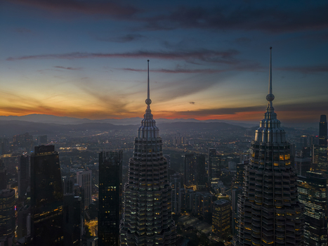 Kuala Lumpur Malaysia 11 March 2026 Aerial view of the Petronas Twin Towers spires against a sunset sky with city lights and distant mountains.
