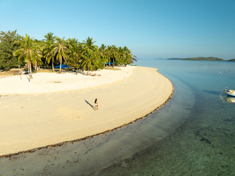 Aerial view of Pass Island featuring a pristine white sand beach lush palm trees and crystal clear turquoise water with a person walking along the shore in Coron Philippines. Aerial view of Pass Island featuring a pristine white sand beach lush palm trees and crystal clear turquoise water with a person walking along the shore in Coron Philippines.