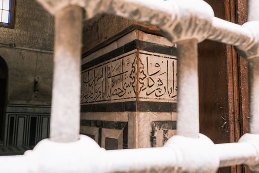 View of the intricate Arabic calligraphy and marble masonry of the Sultan al Ghuri Complex seen through a metal grate El Darb El Ahmar Cairo Governorate Egypt. View of the intricate Arabic calligraphy and marble masonry of the Sultan al Ghuri Complex seen through a metal grate El Darb El Ahmar Cairo Governorate Egypt.