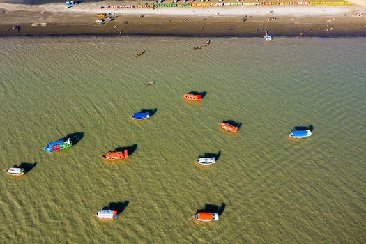 Aerial view of colorful wooden boats floating on the calm water near the sandy beach of Kuakata Barisal Division Bangladesh. Aerial view of colorful wooden boats floating on the calm water near the sandy beach of Kuakata Barisal Division Bangladesh.