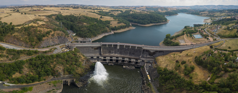 Aerial view of the Barrage de Villerest dam releasing water into the river surrounded by lush green hills and the reservoir in Commelle Vernay Auvergne Rhone Alpes France. Aerial view of the Barrage de Villerest dam releasing water into the river surrounded by lush green hills and the reservoir in Commelle Vernay Auvergne Rhone Alpes France.