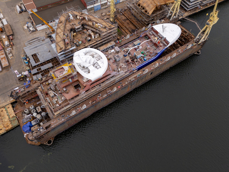 Aerial view of a large ship under construction in a dry dock at a shipyard with industrial cranes and scaffolding in Gdansk Poland. Aerial view of a large ship under construction in a dry dock at a shipyard with industrial cranes and scaffolding in Gdansk Poland.