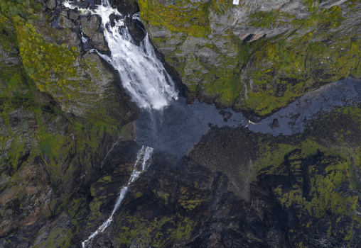 Aerial view of Voringfossen waterfall cascading down steep rocky cliffs with green moss into a dark river canyon in Eidfjord Municipality Vestland Norway.