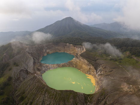 Aerial view of Kelimutu National Park featuring its iconic turquoise and green volcanic crater lakes surrounded by rugged mountain slopes and clouds in Detusoko East Nusa Tenggara Indonesia.