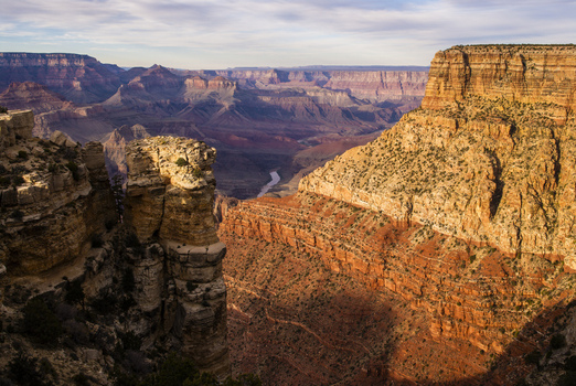 View of the Grand Canyon with rugged rock formations deep gorges and the Colorado River visible in the distance under a soft sunset sky Coconino County Arizona United States. View of the Grand Canyon with rugged rock formations deep gorges and the Colorado River visible in the distance under a soft sunset sky Coconino County Arizona United States.