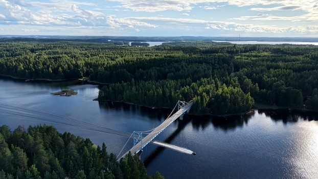 Aerial view of Potkusalmen silta bridge crossing the lake surrounded by dense pine forests with a boat leaving a wake in the water in Savonlinna Etela Savo Finland. Aerial view of Potkusalmen silta bridge crossing the lake surrounded by dense pine forests with a boat leaving a wake in the water in Savonlinna Etela Savo Finland.