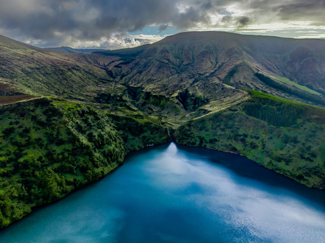 Aerial view of the mirrored surface of the lake reflecting the dramatic sky nestled within the rugged verdant hills of Lake Comprida Flores Azores Portugal.