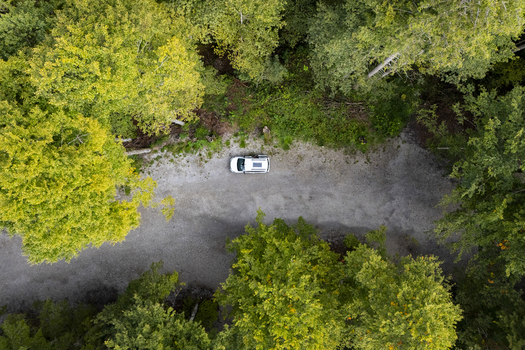Aerial view of a solitary white car parked on a gravel road embraced by verdant trees casting dappled shadows Sylvensteinspeicher Bayern Germany. Aerial view of a solitary white car parked on a gravel road embraced by verdant trees casting dappled shadows Sylvensteinspeicher Bayern Germany.