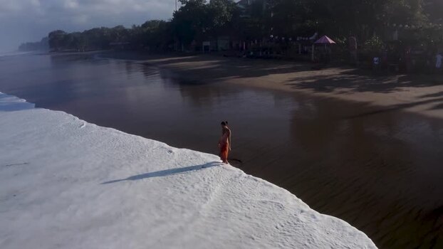Aerial view of a woman walking on a beach with white sea foam Indonesia. Aerial view of a woman walking on a beach with white sea foam Indonesia.