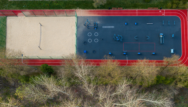 Aerial view of an outdoor sports complex with a red running track sand volleyball court and workout area near green trees Vilnius County Lithuania. Aerial view of an outdoor sports complex with a red running track sand volleyball court and workout area near green trees Vilnius County Lithuania.