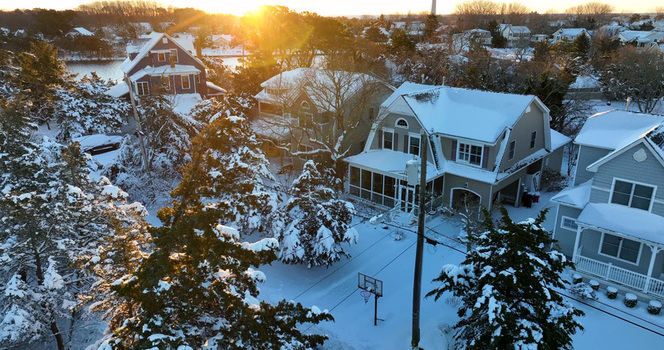 Aerial view of snow covered houses and trees in a residential neighborhood during a golden sunrise in Cape May New Jersey United States.
