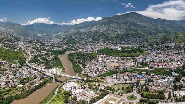 Aerial view of the Neelum River flowing beneath a bridge through the urban landscape surrounded by lush green mountains in Muzaffarabad Azad Kashmir Pakistan. Aerial view of the Neelum River flowing beneath a bridge through the urban landscape surrounded by lush green mountains in Muzaffarabad Azad Kashmir Pakistan.