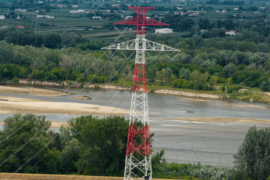 Aerial view of a red and white high voltage electricity pylon standing near a river with sandy banks and lush green trees in Poland. Aerial view of a red and white high voltage electricity pylon standing near a river with sandy banks and lush green trees in Poland.