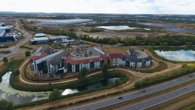 Aerial view of the unique architecture of Wixams Retirement Village featuring curved buildings surrounded by lakes and green spaces in Bedford England United Kingdom.