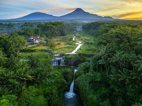 Aerial view of Grojogan Watu Purbo multi tiered waterfall surrounded by lush tropical greenery with Mount Merapi in the background during sunrise Kecamatan Tempel Daerah Istimewa Yogya Indonesia.