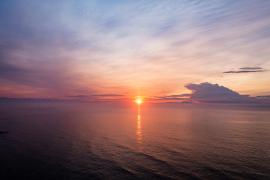 Aerial view of the sun rising over the Atlantic Ocean at Sea Isle City Beach with soft clouds and calm water reflecting the golden light in Sea Isle City New Jersey United States.
