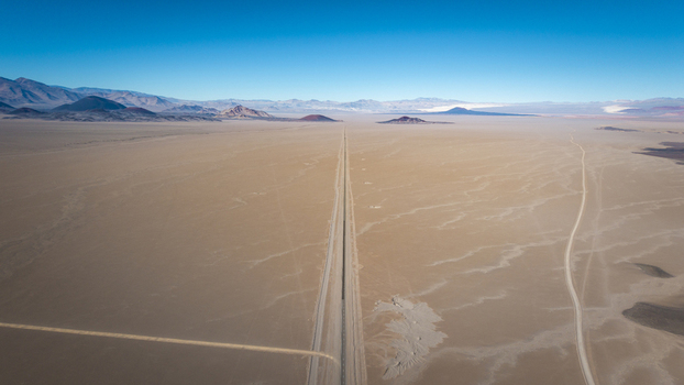 Aerial view of a long straight road cutting through the vast arid desert landscape under a clear blue sky in Argentina. Aerial view of a long straight road cutting through the vast arid desert landscape under a clear blue sky in Argentina.