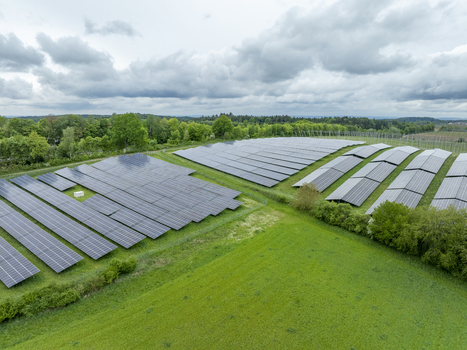 Aerial view of a solar farm with rows of photovoltaic panels surrounded by green meadows and lush forests under a cloudy sky in Aiglsbach Bavaria Germany.