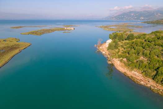 Aerial view of the turquoise waters of Kanali i Vivarit flowing between lush green banks and small islands under a clear sky in Vrine Vlore County Albania. Aerial view of the turquoise waters of Kanali i Vivarit flowing between lush green banks and small islands under a clear sky in Vrine Vlore County Albania.