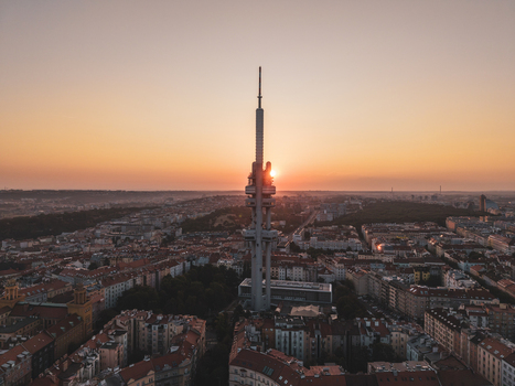 Aerial view of Zizkov Television Tower rising above the historic rooftops and urban landscape of the city during a warm golden sunset in Prague Hlavni mesto Praha Czechia.