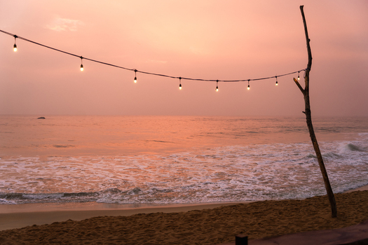 View of a beach at sunset with a string of glowing decorative lights hanging from a wooden pole over the sandy shore Galle Southern Province Sri Lanka.