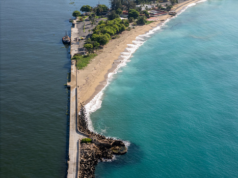 Aerial view of the Rio Ozama meeting the Caribbean Sea with a long concrete pier sandy beach and lush green trees along the coastline Santo Domingo Santo Domingo Dominican Republic.