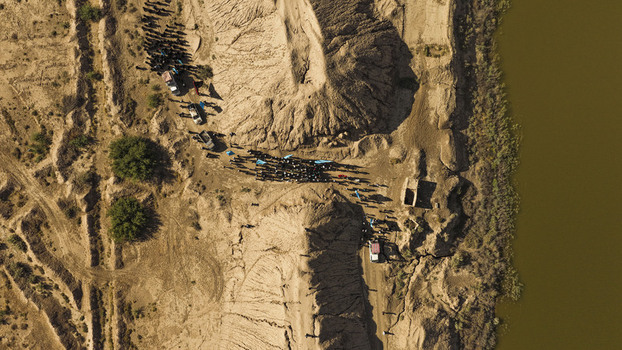 Aerial view of a group of people gathered near vehicles in a desert landscape with sandy mounds and a riverbank in Al Budayr Al Qadisiyah Governorate Iraq.