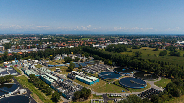 Aerial view of a wastewater treatment plant with circular sedimentation tanks and industrial buildings surrounded by green fields and trees in Milan Lombardy Italy. Aerial view of a wastewater treatment plant with circular sedimentation tanks and industrial buildings surrounded by green fields and trees in Milan Lombardy Italy.
