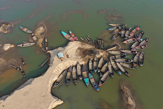 Aerial view of numerous wooden boats moored along the sandy banks of the Jadukata River showcasing the intricate patterns of the waterway in Sunamganj Sylhet Division Bangladesh. Aerial view of numerous wooden boats moored along the sandy banks of the Jadukata River showcasing the intricate patterns of the waterway in Sunamganj Sylhet Division Bangladesh.