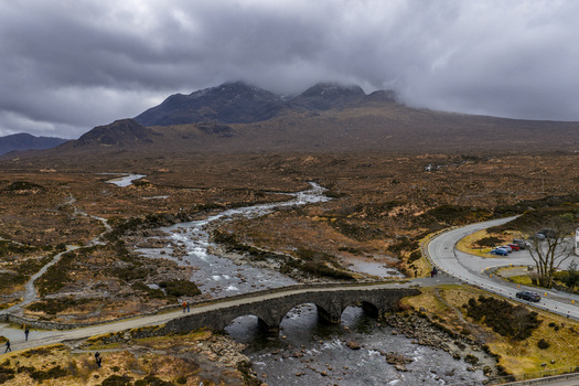 Aerial view of Sligachan Old Bridge crossing a rocky river with the Cuillin Hills under a dramatic cloudy sky in Sligachan Scotland United Kingdom. Aerial view of Sligachan Old Bridge crossing a rocky river with the Cuillin Hills under a dramatic cloudy sky in Sligachan Scotland United Kingdom.