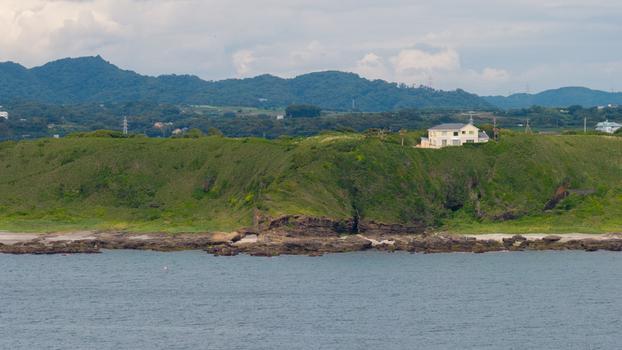 Aerial view of a house perched on a grassy cliff overlooking the rocky coastline and the sea in Japan. Aerial view of a house perched on a grassy cliff overlooking the rocky coastline and the sea in Japan.