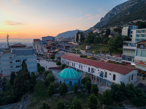 Aerial view of the historic town center with a green domed building red roofed houses and the rugged slopes of Mount Kruje at sunset in Kruje Durres County Albania.